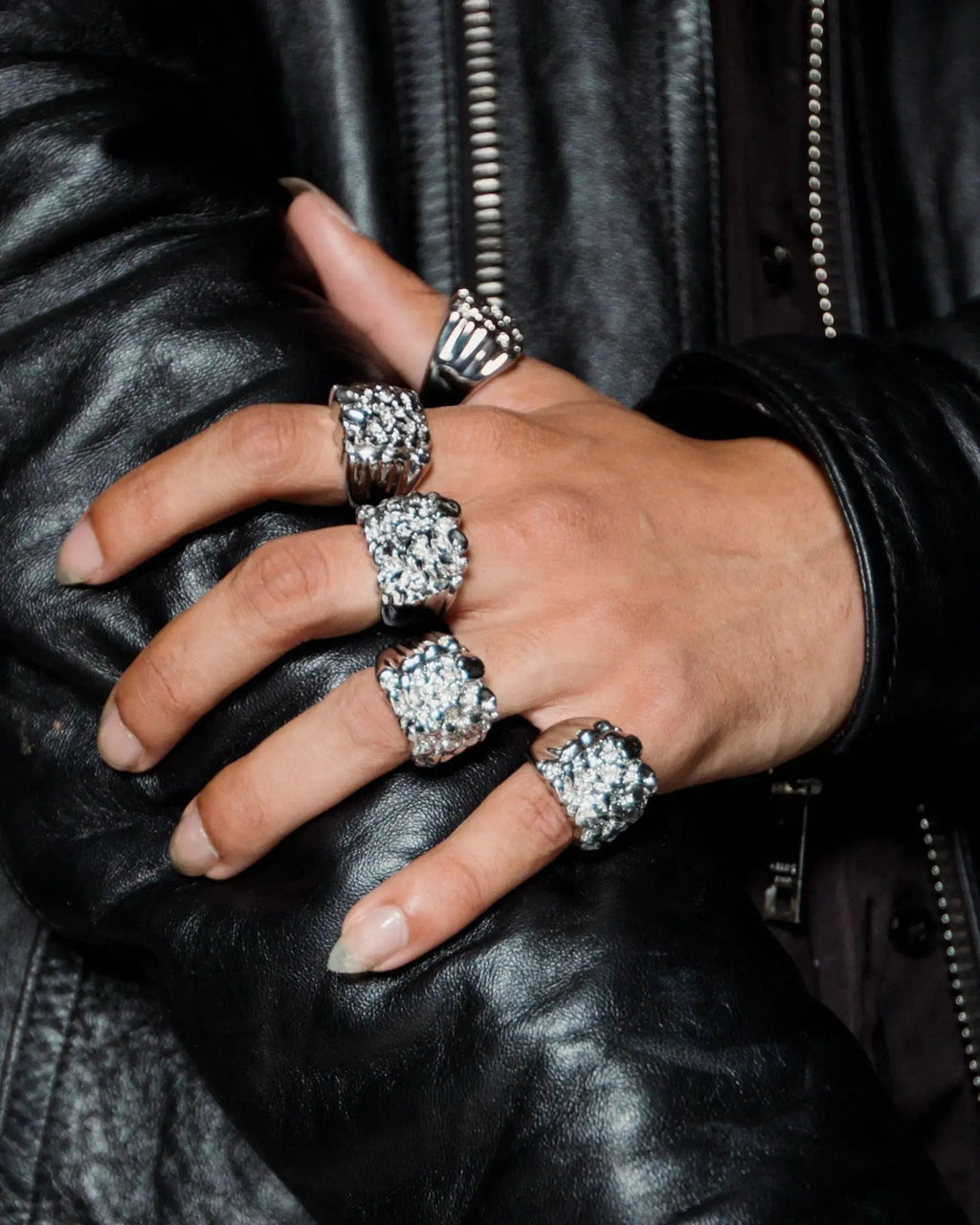 Hand wearing multiple silver rings on a black leather jacket background