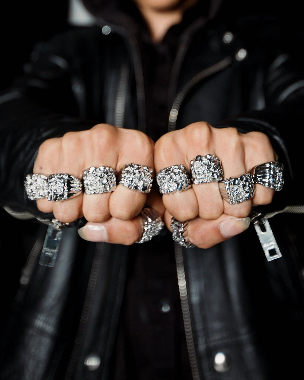 Close-up of fists wearing multiple silver rings on a black background
