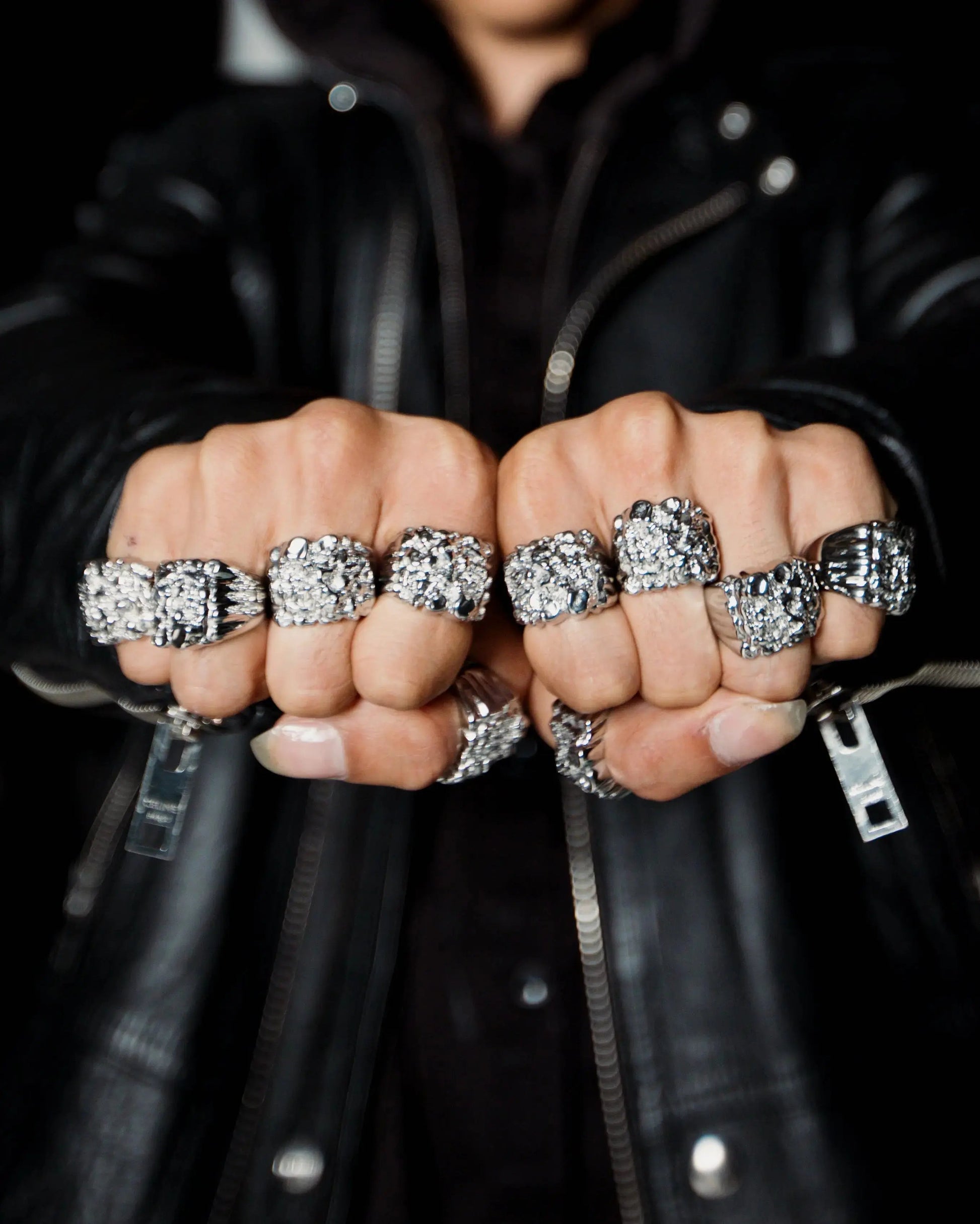 Close-up of fists wearing multiple silver rings on a black background
