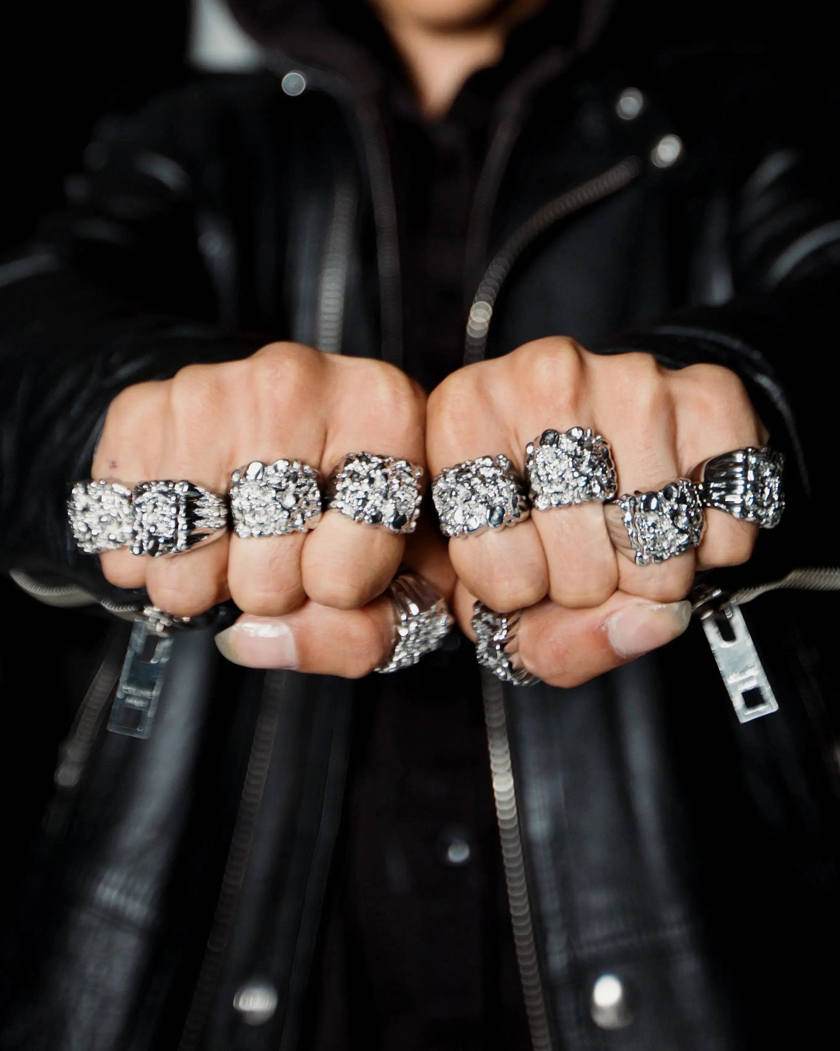 Close-up of fists wearing multiple silver rings on a black background