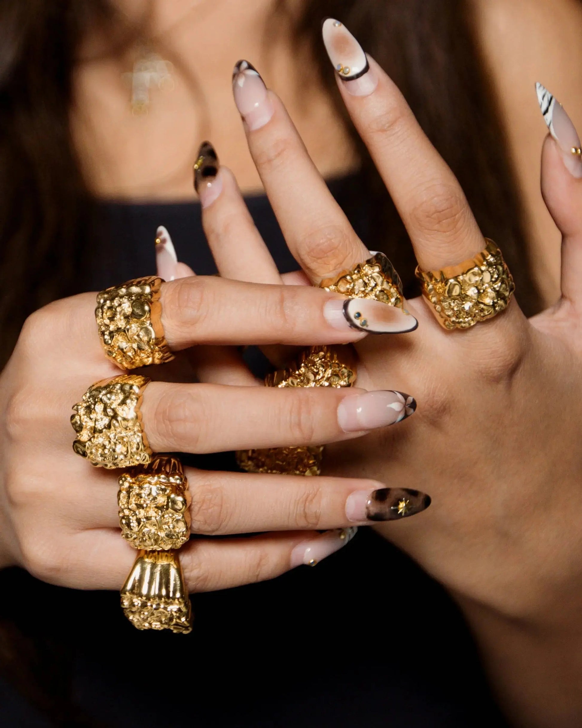 Close-up of a hand wearing multiple gold rings with a dark background