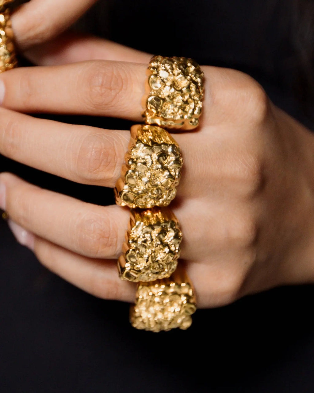 Close-up of a hand wearing two gold rings with a textured design on a black background