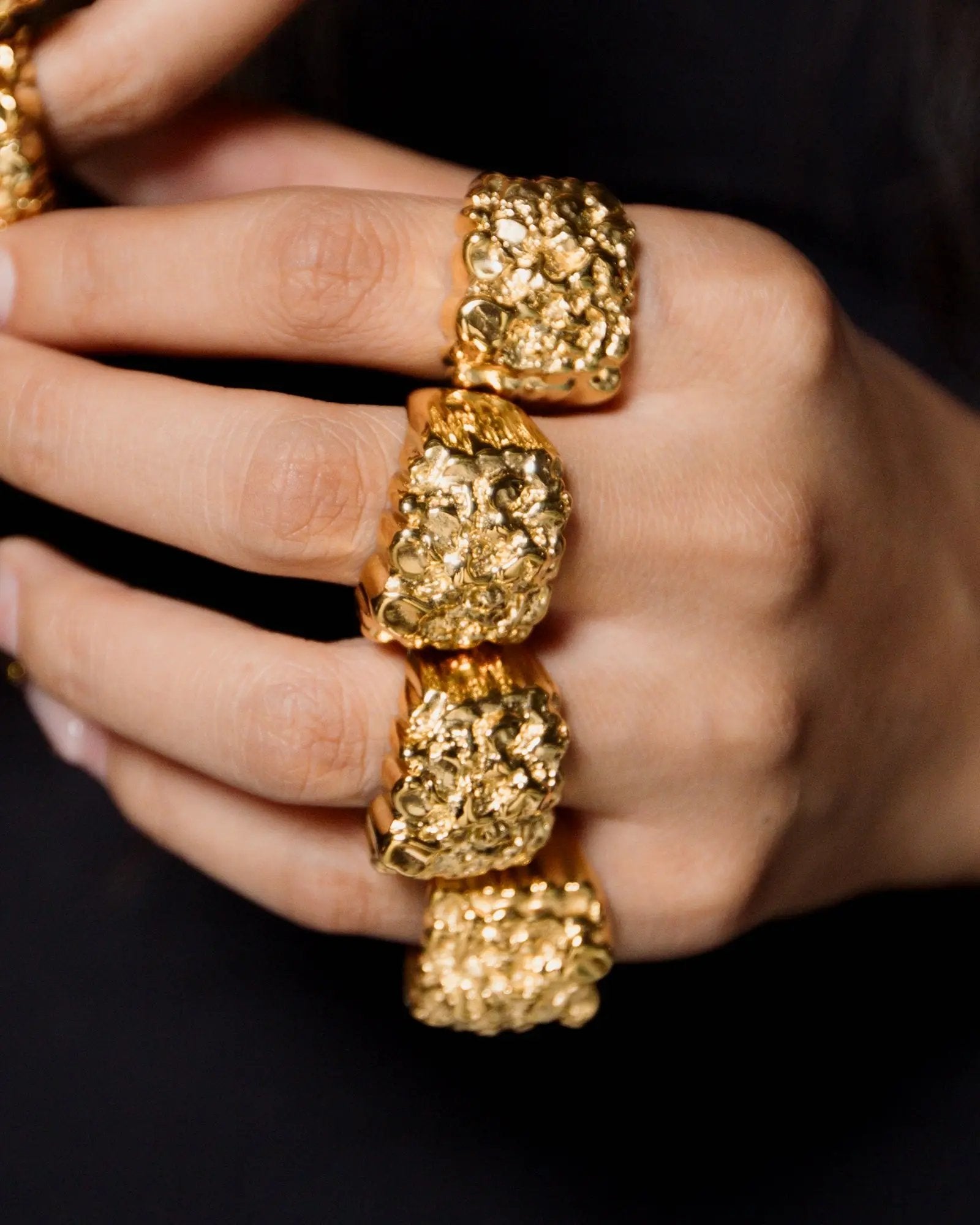 Close-up of a hand wearing two gold rings with a textured design on a black background
