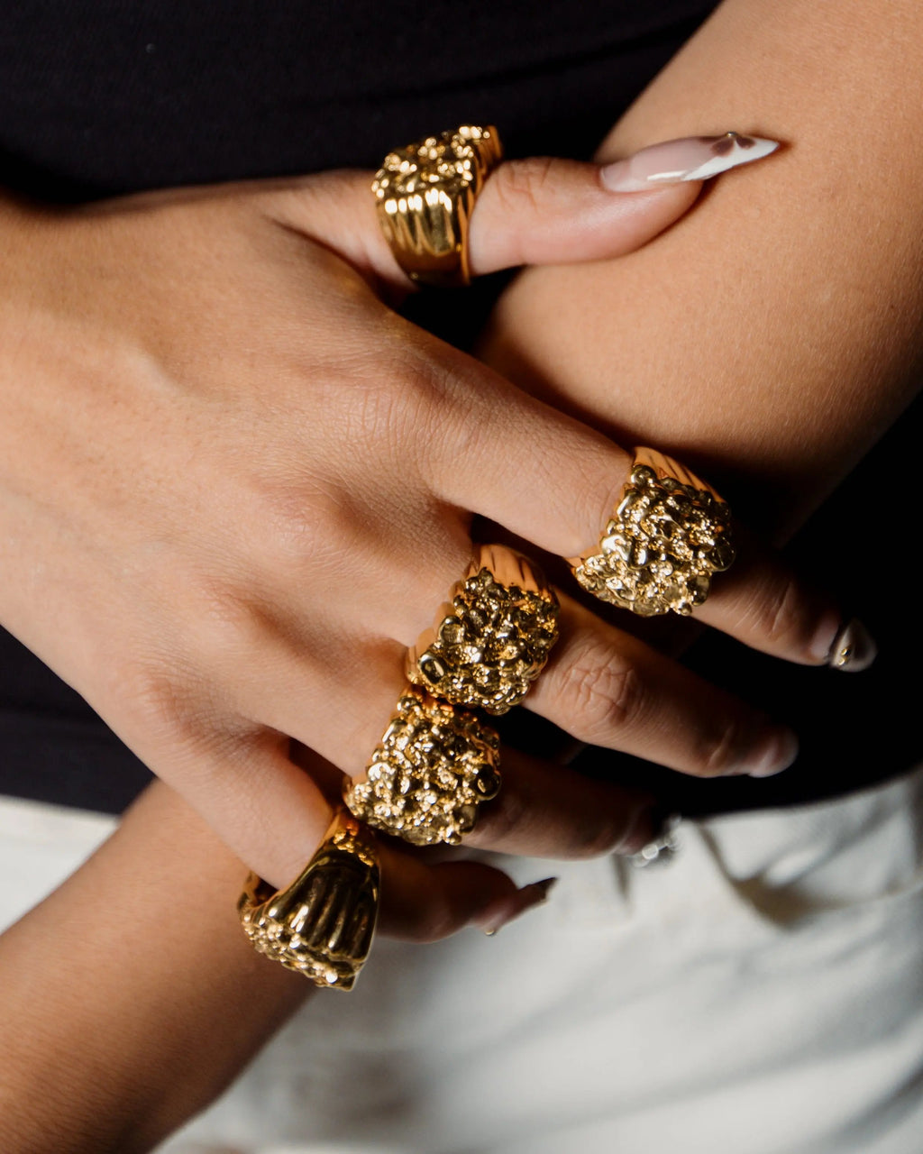Close-up of a hand wearing multiple gold rings with a blurred background
